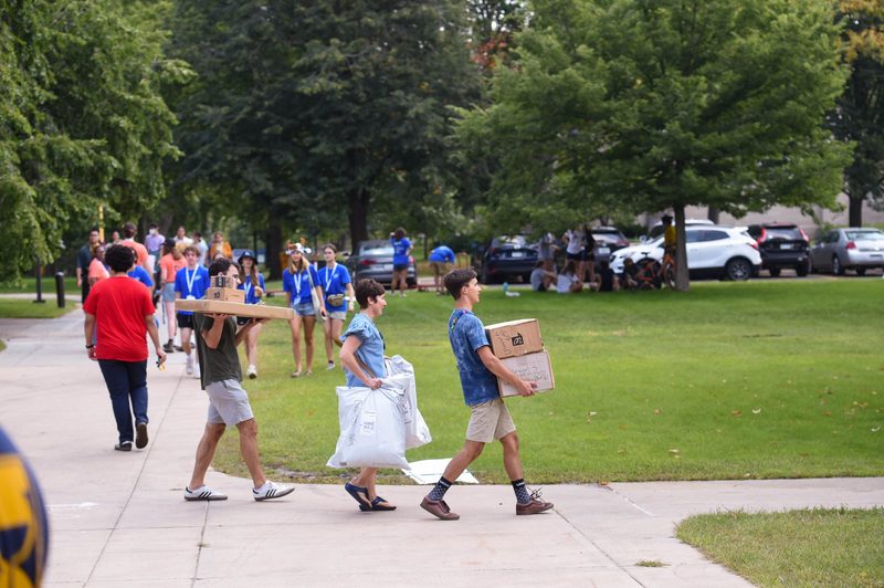 A student and their family carry multiple packages across a sidewalk.