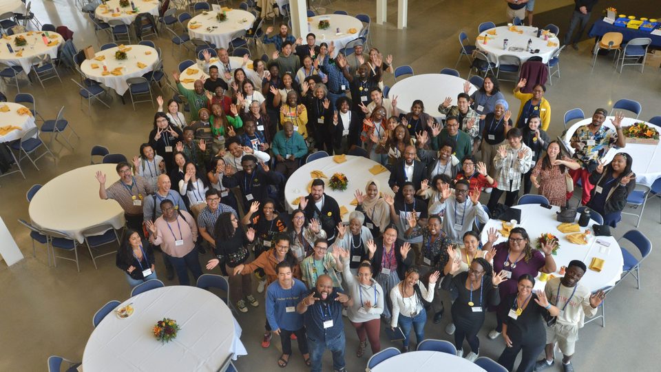 Photo from above. A large group of alumni and students of color wave up at the camera from the Weitz Commons.