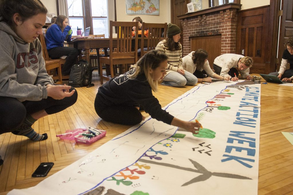 Students draw symbols of sustainability with markers on a large sheet of butcher paper spread out on the floor. Paper reads "Climate Action Week."