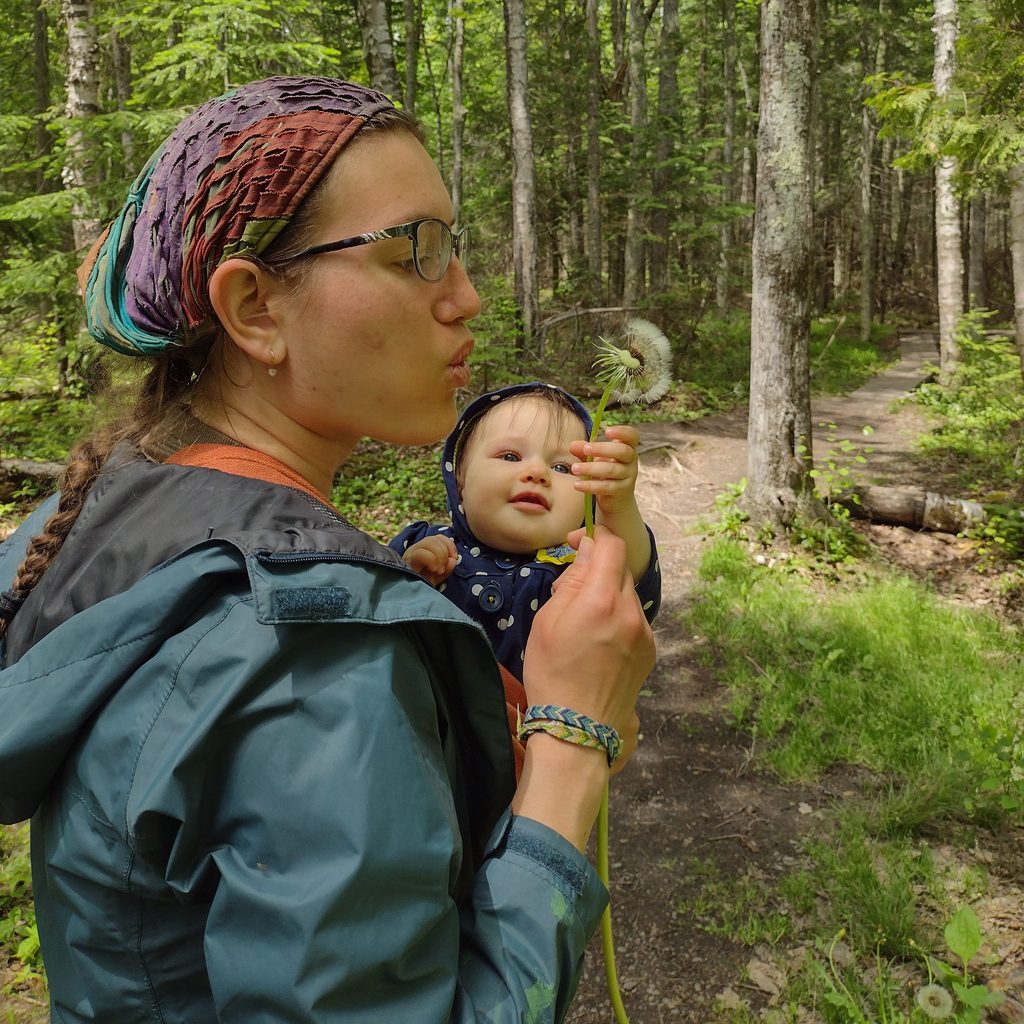 Mikhalina Solakhava ’23 carries a baby in the forest and blows on a dandelion.