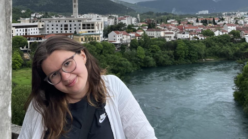 Mia Strubel Iram poses with a river and city landscape in the background.