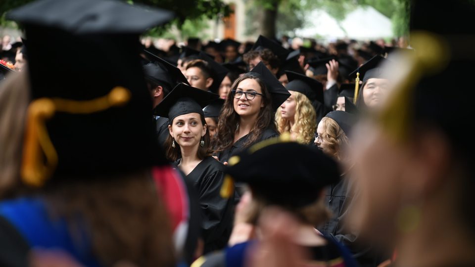 Focus on one student smiling amongst a sea of graduating students.