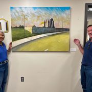 Theresa Nash ’73 and Pierre Montant smile and gesture to the picturesque painting hanging on the wall between them.