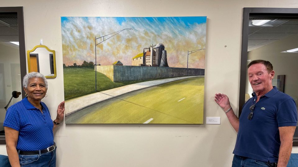 Theresa Nash ’73 and Pierre Montant smile and gesture to the picturesque painting hanging on the wall between them.