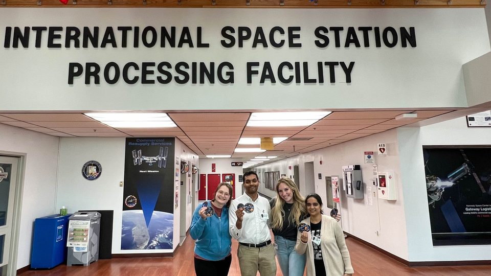 Four people pose together under a sign reading