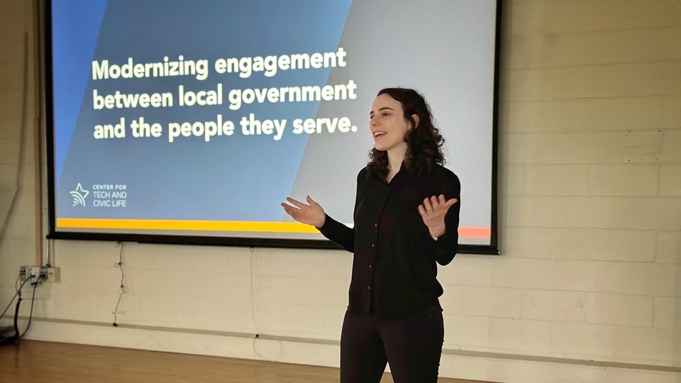 Sarah Berlin gesturing in front of a projector with a slide reading