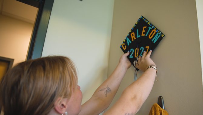 A new student hangs their high school graduation cap, which is decorated with the words 