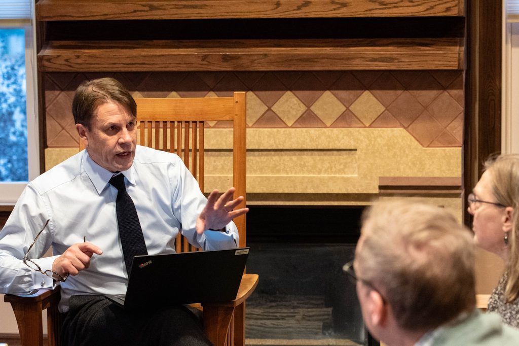 Professor Tim Raylor gestures as he speaks to two other professors, all of them sitting in chairs.