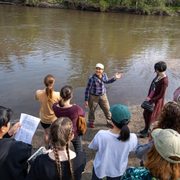 Nancy Braker gestures behind her to the Cannon River as she talks to a group of students.