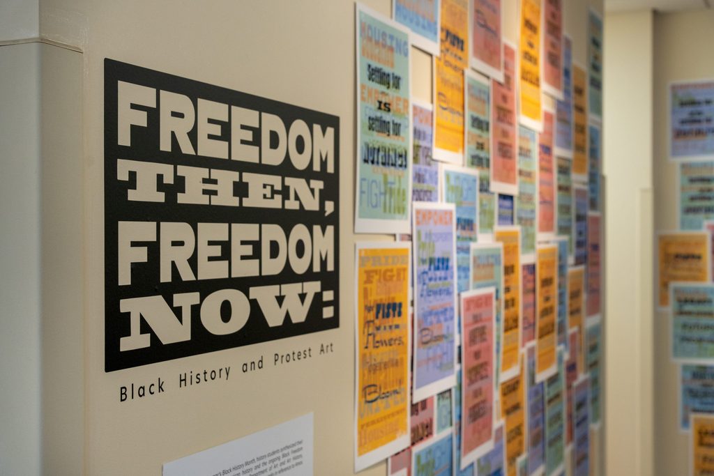 Colorful posters hanging up next to a sign that reads "Freedom Then: Freedom Now"