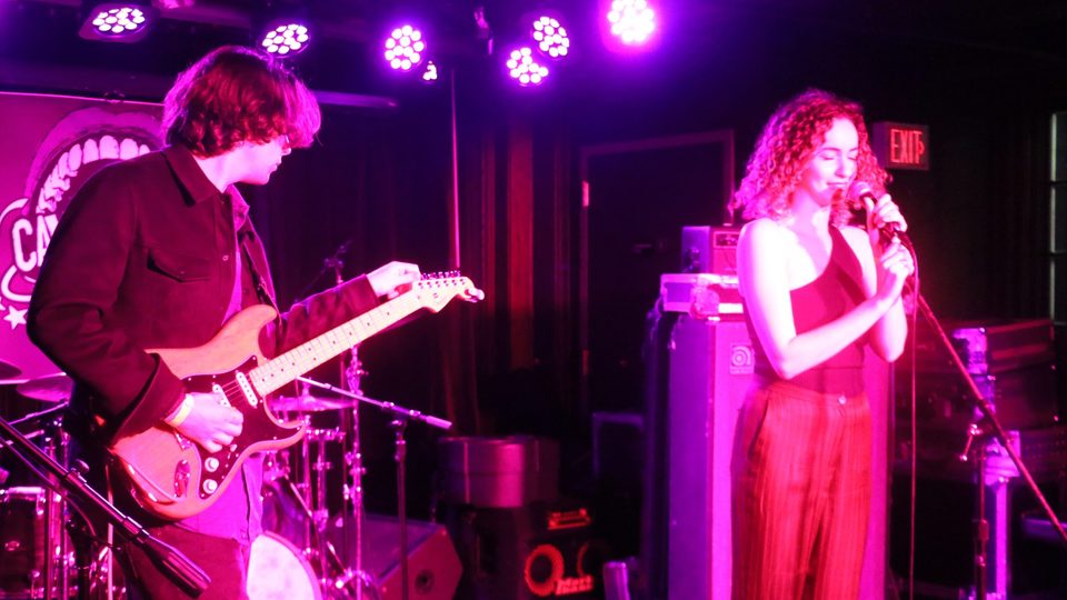 Rebecca McCartney singing into microphone accompanied on stage by bass guitarist