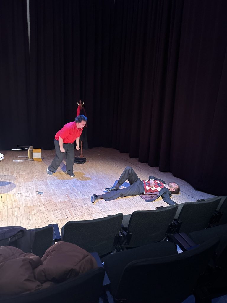 Le as Cruncher screams at Preves as Louis, who is collapsed on the stage.