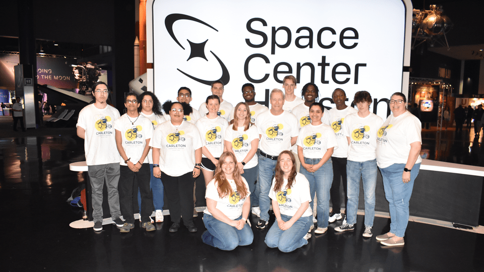 Students and staff posing for a group photo in front of the Space Center Houston sign.