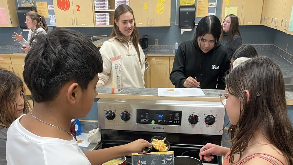 Students stand at a stove, cooking