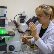 Student in white lab coat looking through a microscope in the lab