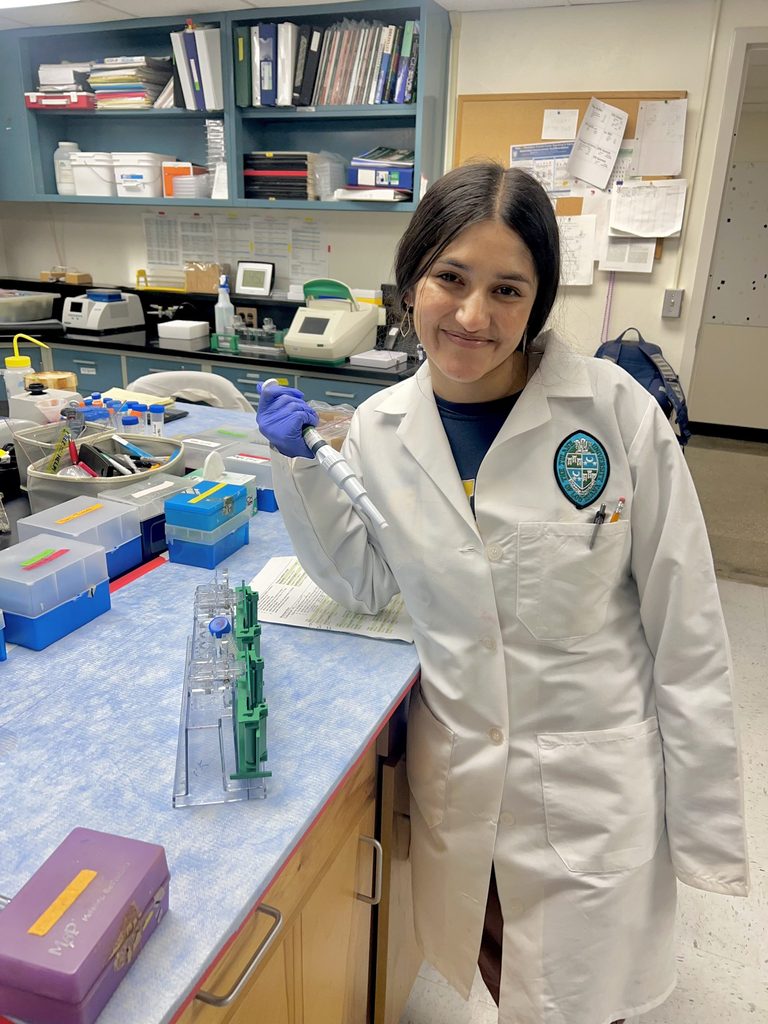 Chanda posing next to lab equipment, smiling at the camera