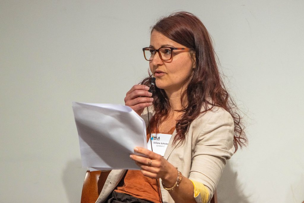Juliane Schicker speaks into a lapel microphone while holding up a packet of paper.