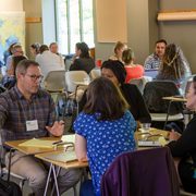 A large collection of small groups of people talk in a classroom.