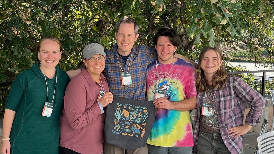 Five people pose outdoors with a BeaverCON tote bag.