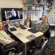 Claire Kelling and a group of students sitting around a table smile at the camera.
