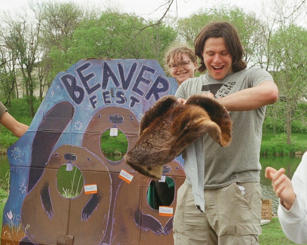 Jonah Docter-Loeb holds a beaver pelt in front of a sign advertising Beaver Fest on Carleton's campus