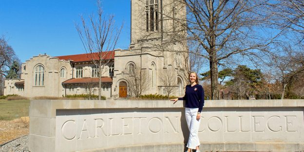 Anna Ursin ’25 standing in front of the Carleton sign by the Chapel.