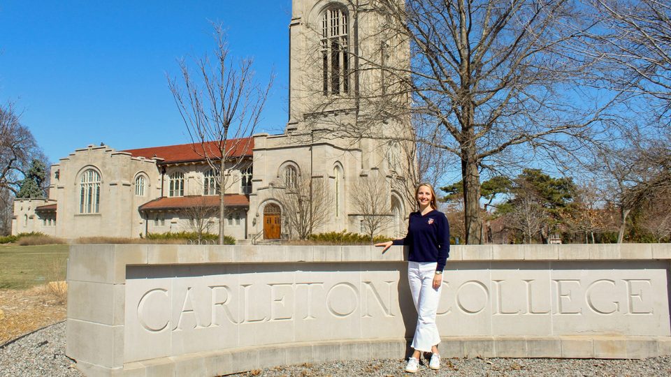 Anna Ursin ’25 standing in front of the Carleton sign by the Chapel.