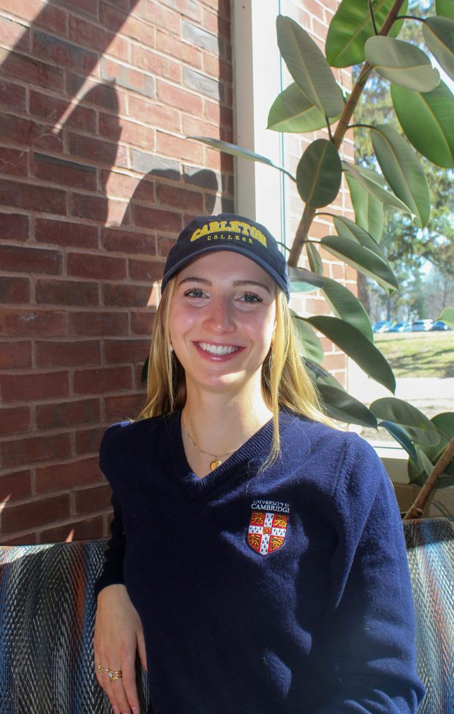 Headshot of Anna Ursin ’25 wearing a Carleton hat and a University of Cambridge sweater.