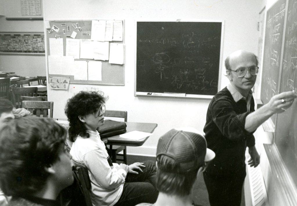 Black and white photo of Russ Petricka using a blackboard to explain something to students.