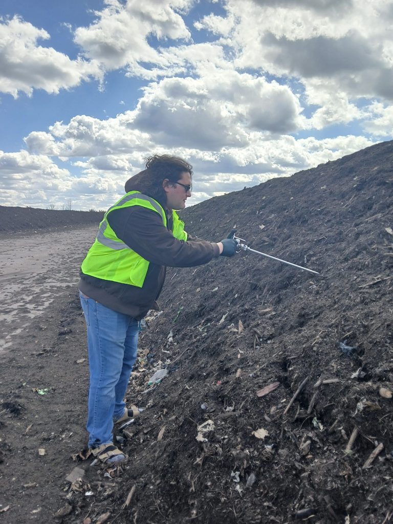 Student stands next to pile of compost