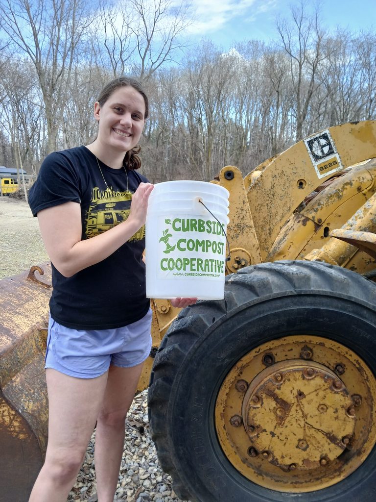 Person standing next to yellow tractor holding white bucket