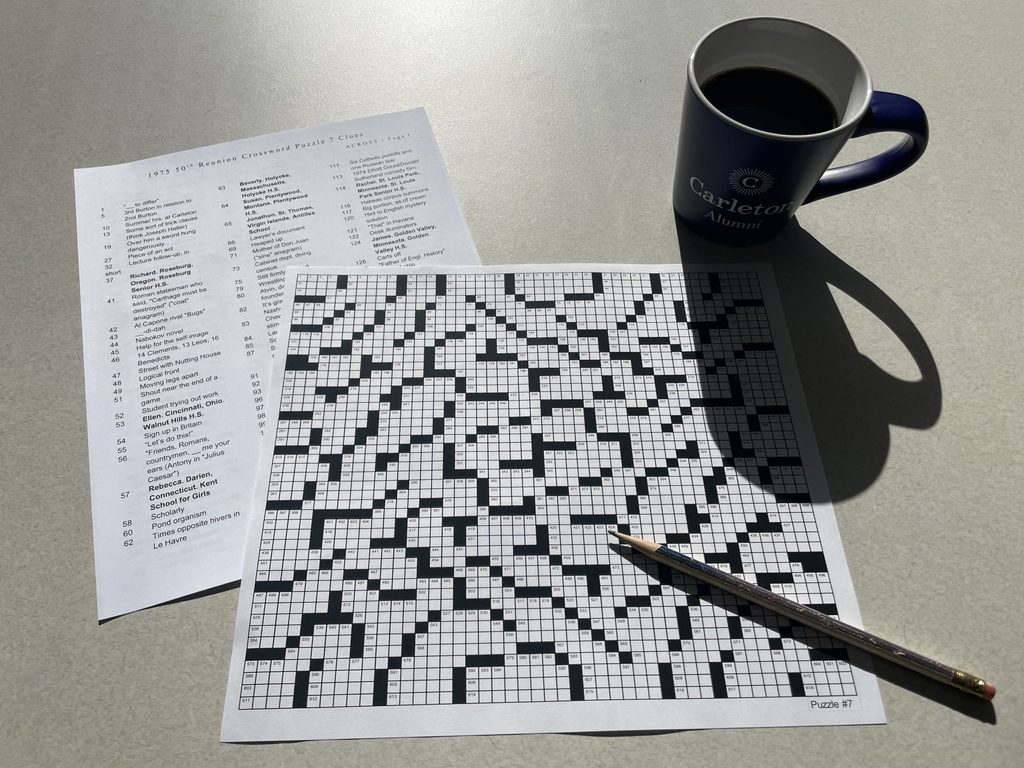 A pencil and a coffee mug reading, "Carleton Alumni" sit on top of a large crossword puzzle.