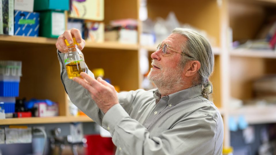 Brian Fox ’81 holds up a container of liquid in a lab.