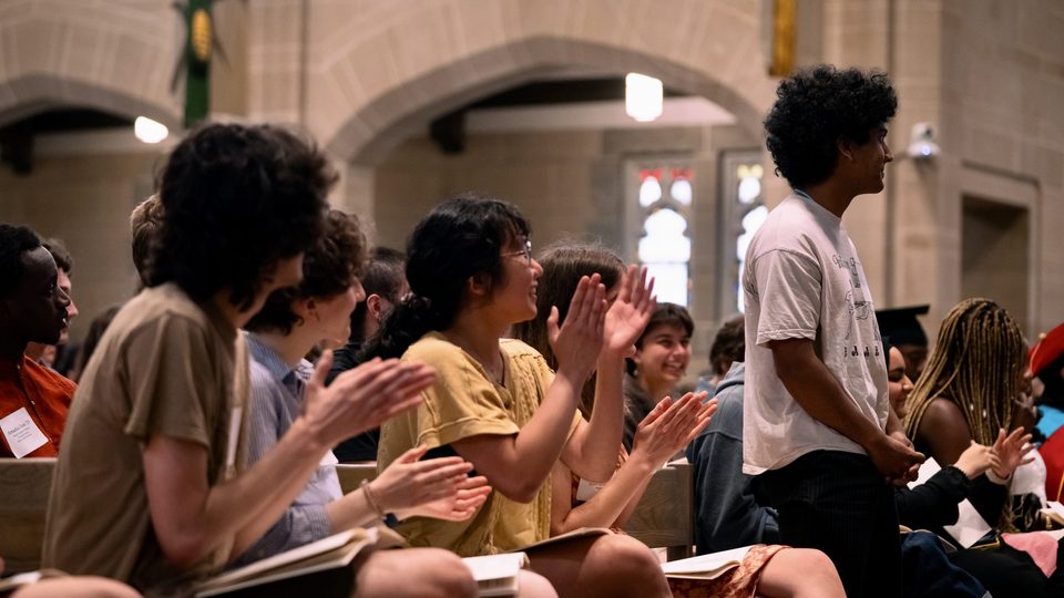 A student stands up in an applauding crowd at Honors Convo.