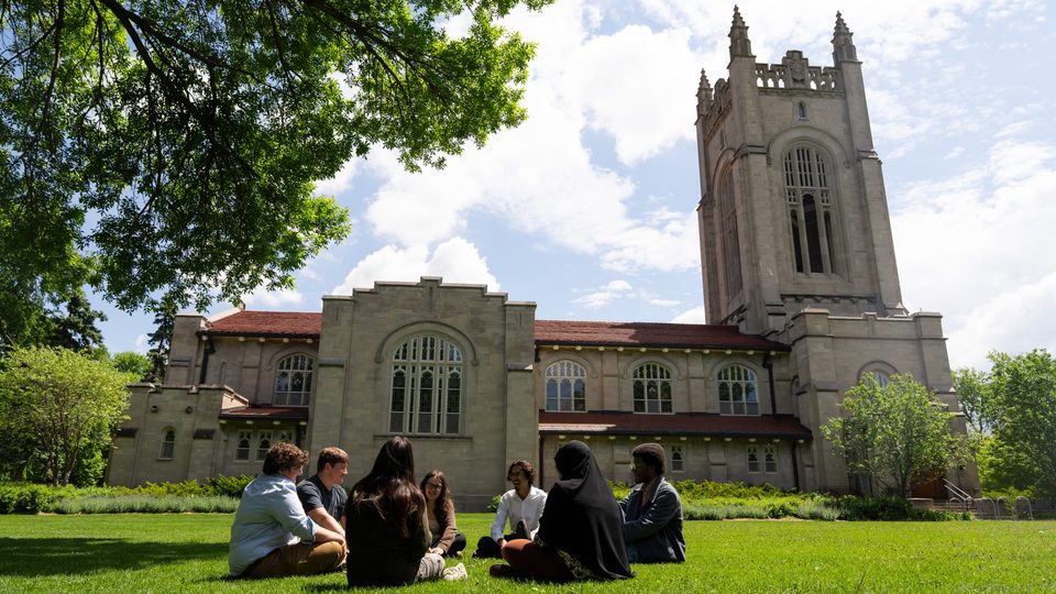 A group of students sit in a circle by the Chapel on a sunny day.