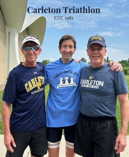 Three people in Carleton shirts smile at the camera with their arms around each other. The top of the photo has text reading, "Carleton Triathlon EST. 1981."