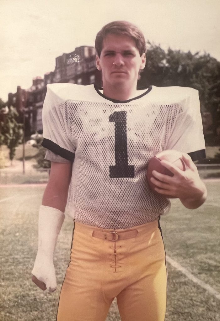 John Winter ’85 in his Carleton football uniform, holding a football.