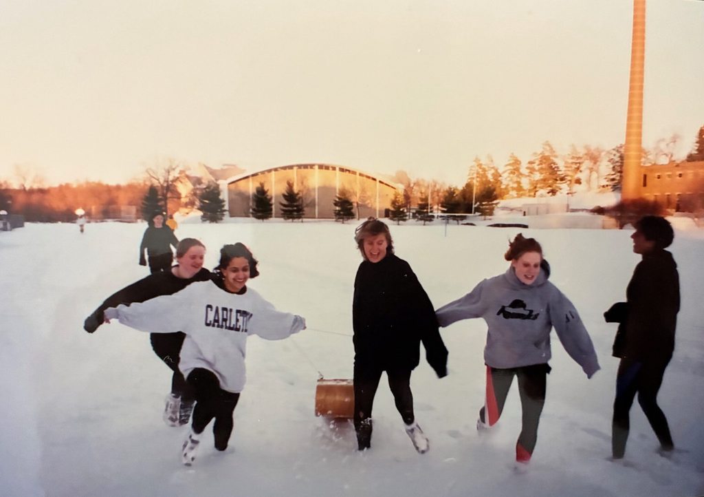 Students frolic and pull a sled through snow on the Laird Stadium field.