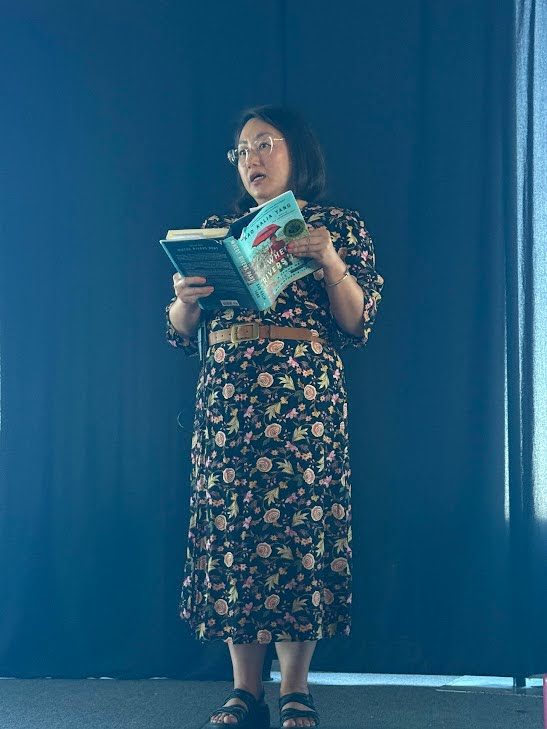 Kao Kalia Yang stands on a stage and reads from one of her books.