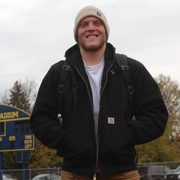Jack Curtis stands in front of the Carleton Football scoreboard on a cloudy day.