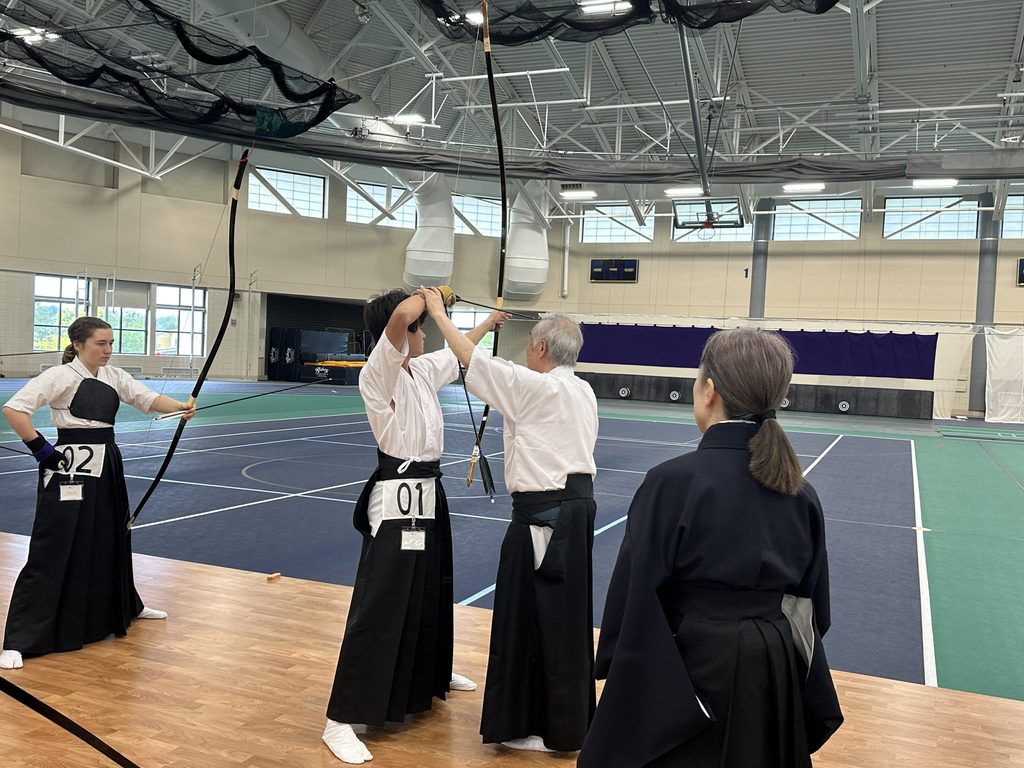 Kyudo practitioner shooting a bow while being corrected by an instructor