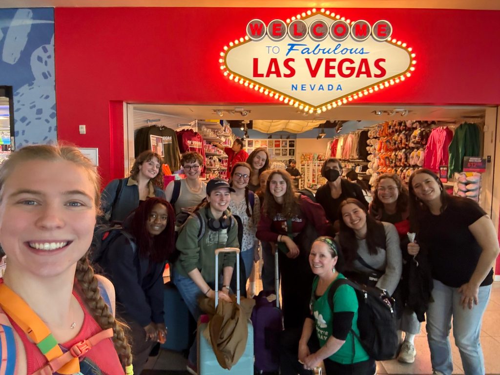 A person takes a selfie with a group in front of a gift shop labeled, "Welcome to Fabulous Las Vegas, Nevada."