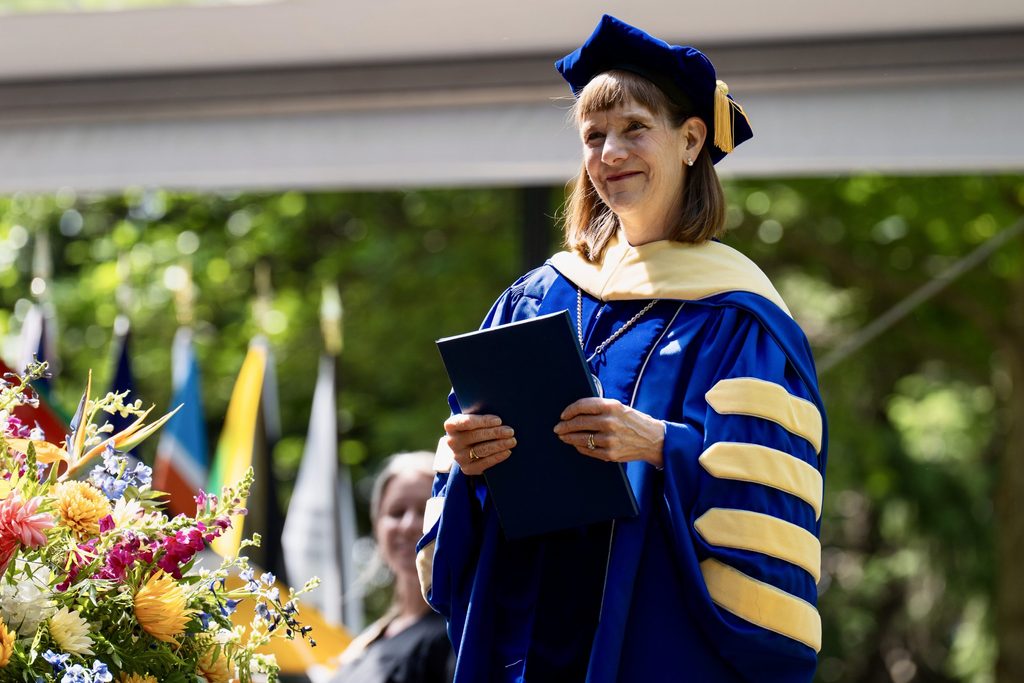 Alison Byerly smiles as she holds a student's diploma during Commencement 2026.