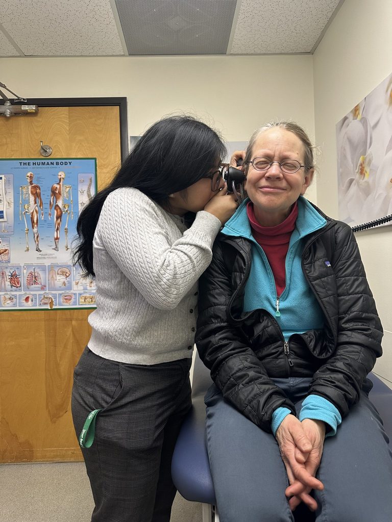 A student playfully looks into the ear of her boss with an otoscope in a doctor's office.