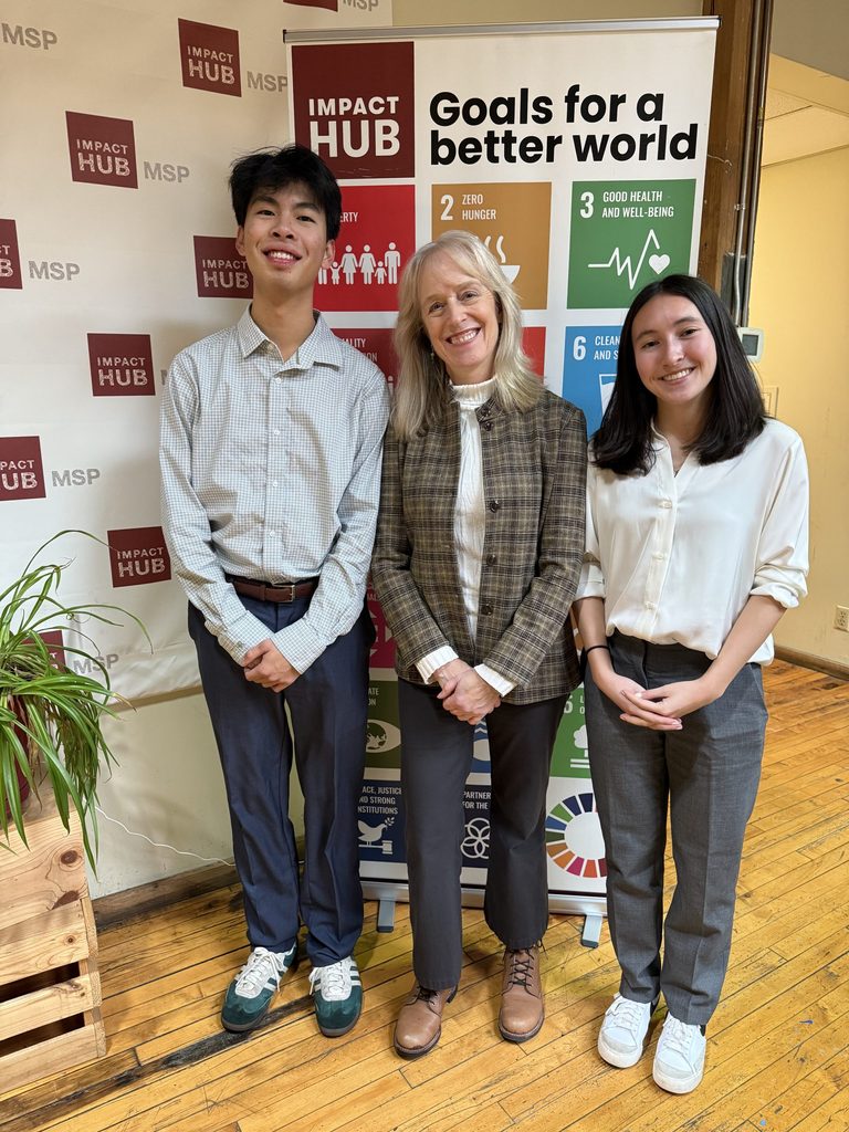 Two students pose with an alum in front of a sign for "Impact Hub."