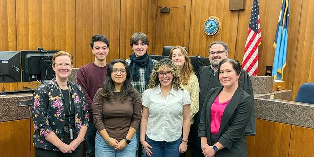 A group of students and professionals pose in a court room.