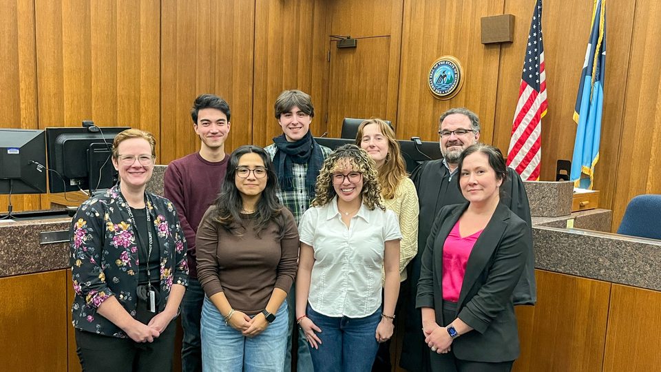 A group of students and professionals pose in a court room.