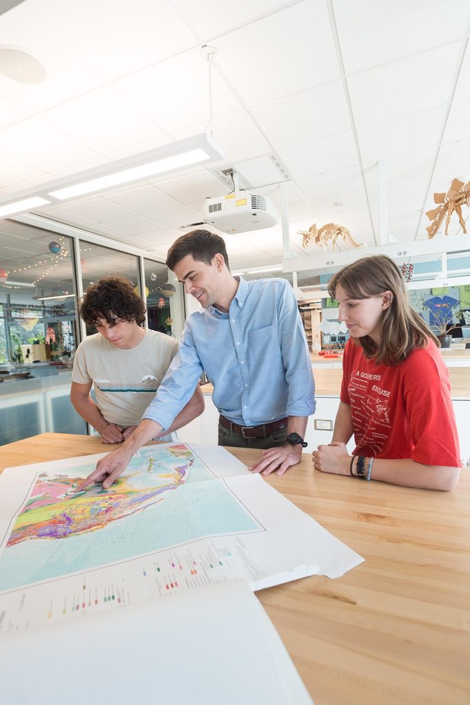 A professor points something out on a map to two students in an Anderson Hall lab.