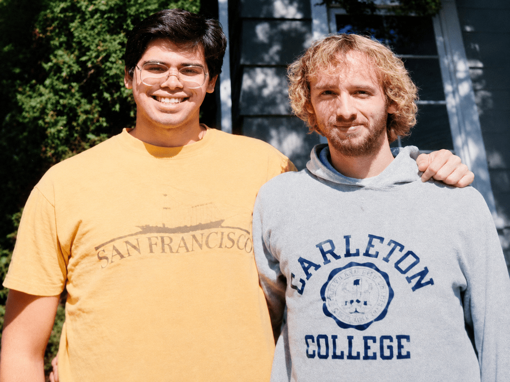 David Wallace-Jackson and Dan Tysver, who is wearing a Carleton sweatshirt, pose together with their arms around each other.