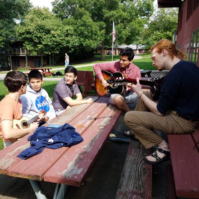 Five RAs having a jam session. Two have guitars and one has a ukulele.